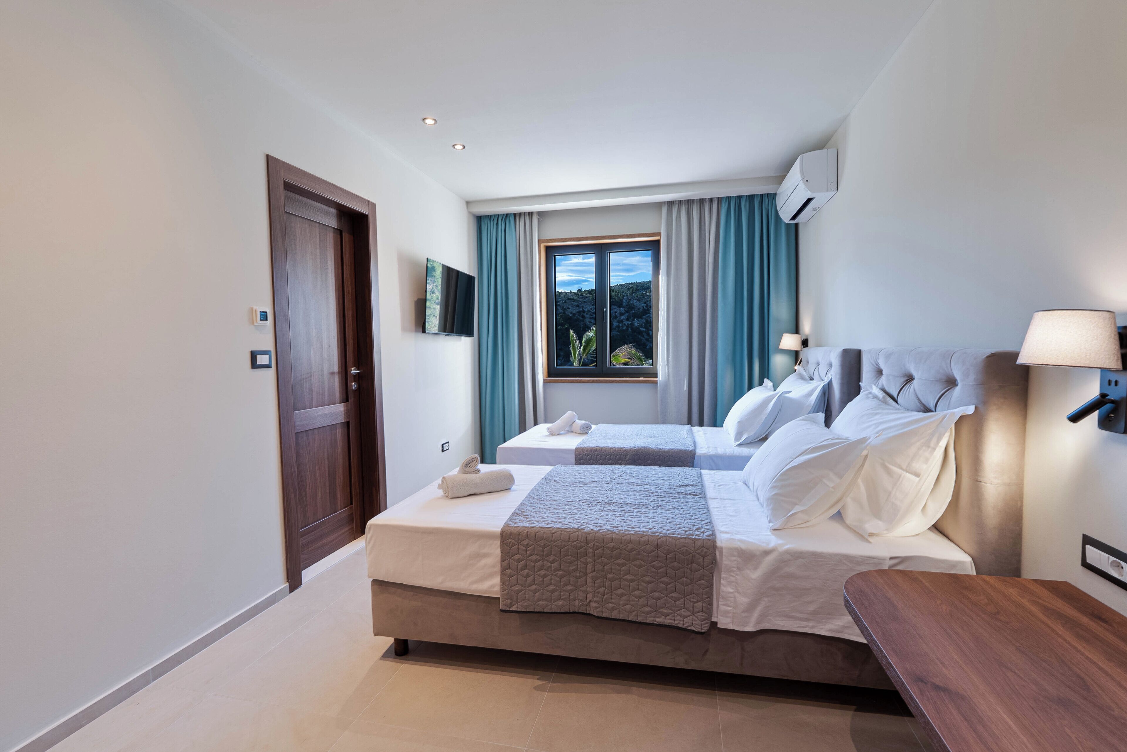 Une chambre d’hôtel avec deux lits, une télévision, une fenêtre avec des rideaux et une table de chevet.