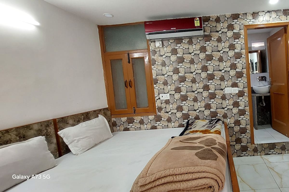 A bedroom with a bed, a wardrobe, a bathroom with a toilet and sink, and a TV mounted on the wall.