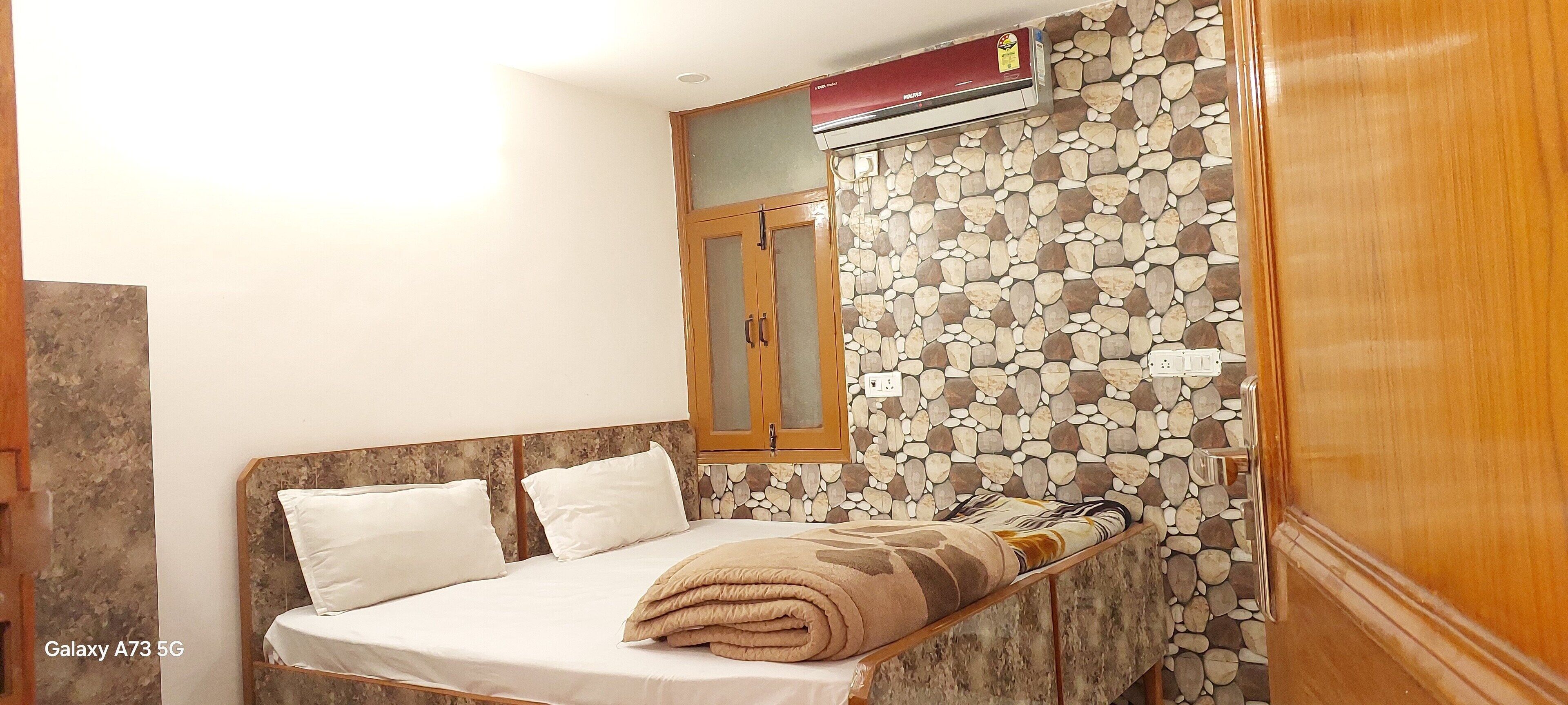 Un dormitorio con cama, un armario de madera, una pared con diseño de piedra y aire acondicionado instalado en el techo.