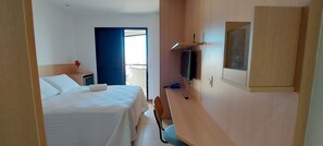 Une chambre d’hôtel équipée d’un lit, d’un bureau, d’une télévision et d’une porte donnant sur un balcon.