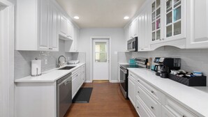 A modern kitchen with white cabinetry, a microwave, a coffee maker, and a dishwasher. - Midcentury Marvel 5-bedroom pool house – walk to UF Stadium & Campus (Gainesville)