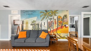 A living room with a gray sofa, orange throw pillows, a wooden coffee table, and a colorful mural on the wall. - Midcentury Marvel 5-bedroom pool house – walk to UF Stadium & Campus (Gainesville)