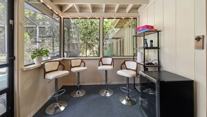 A room with three bar stools, a black cabinet, and a potted plant by the window. - Midcentury Marvel 5-bedroom pool house – walk to UF Stadium & Campus (Gainesville)