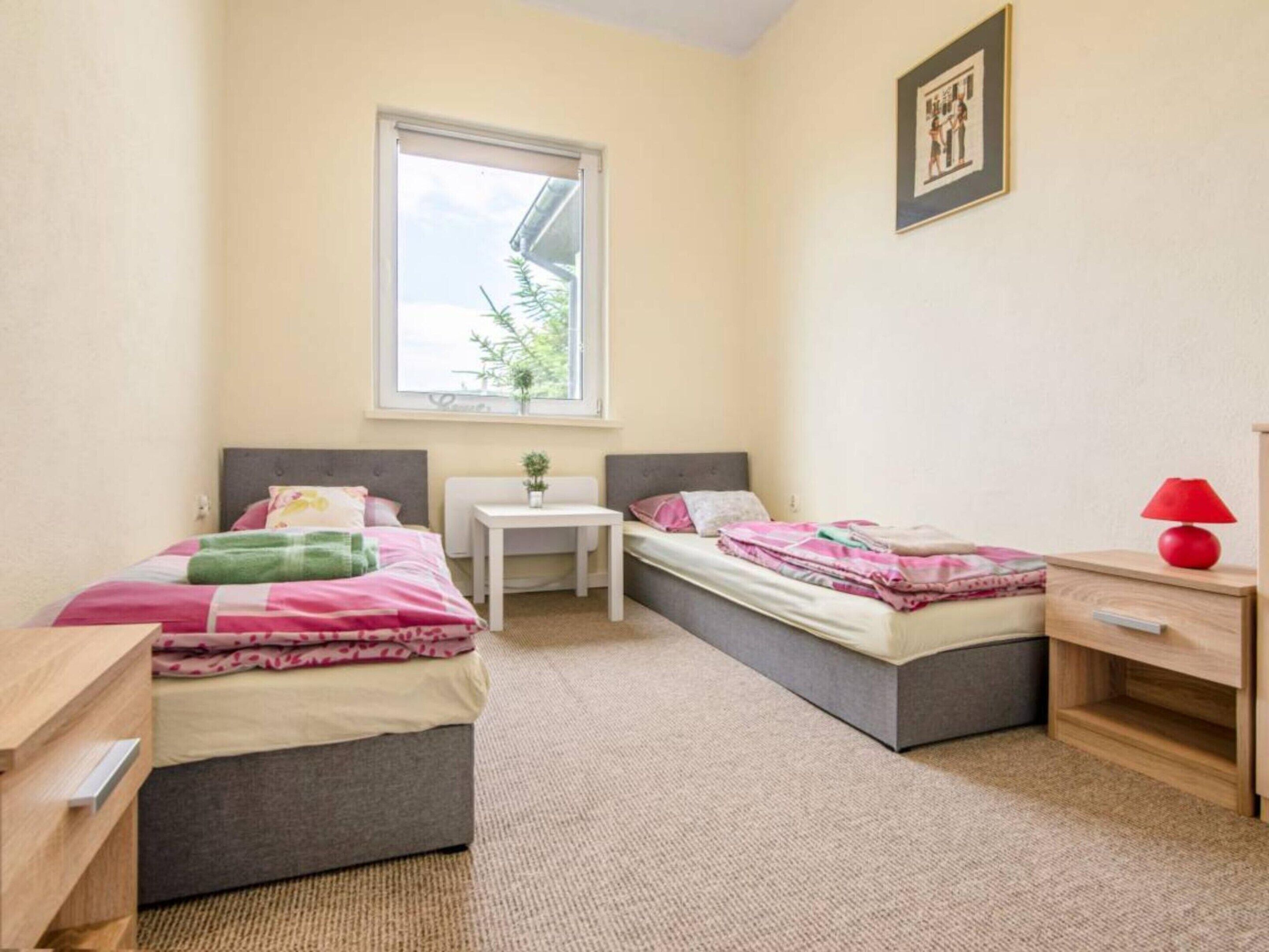 Una camera da letto con due letti, un tavolino, un comodino, una finestra e un quadro appeso al muro.