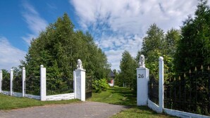A gated entrance with a paved pathway leading to a building, surrounded by lush greenery and a clear sky. - Luxurious Holiday Home With Swimming Pool (gmina Dobra)