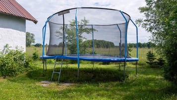 Un trampolín con red de seguridad, situado en un césped con un edificio blanco al fondo.