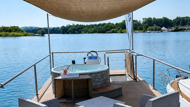 Dæk på en båd med jacuzzi, fletmøbler og et markise.