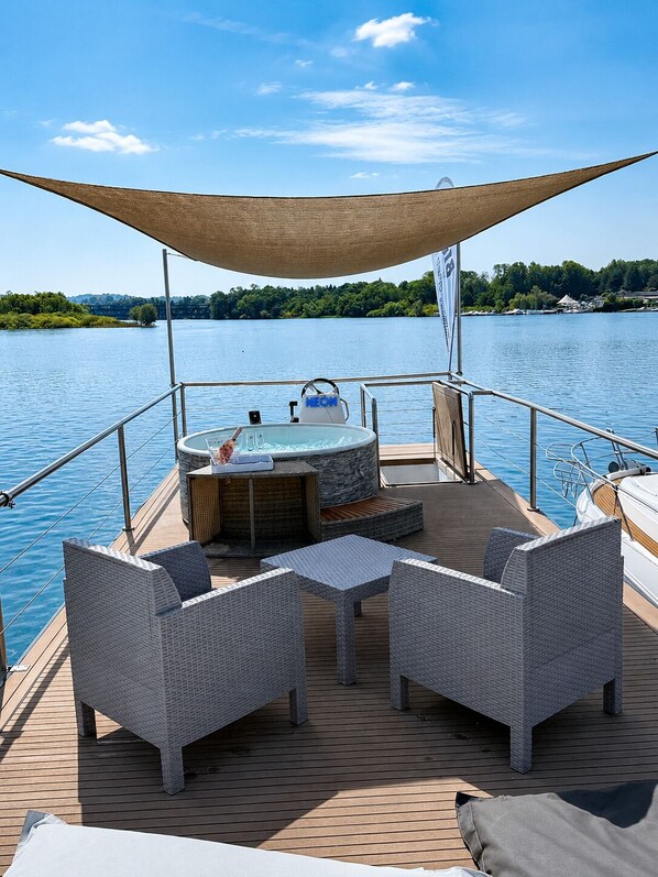 A boat deck with a hot tub, wicker furniture, and a canopy.