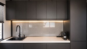 Et moderne køkken med mørke skabe, en hvid bordplade, en sort hane og en kaffemaskine.