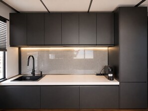 Une cuisine moderne avec des meubles de couleur sombre, un plan de travail blanc, un robinet noir et une machine à café.