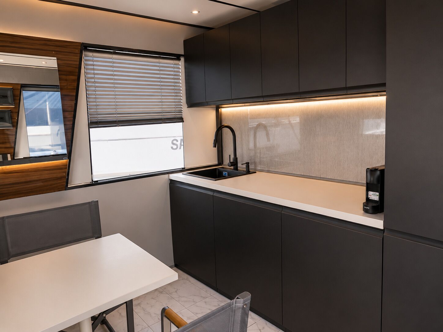 Una cucina moderna con mobili scuri, un piano di lavoro bianco, un rubinetto nero e una macchina per il caffè.