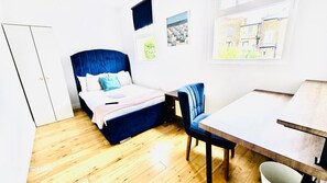 A bedroom with a bed, a chair, a table, and two windows. - Room 5 in Camden Parkway (London)