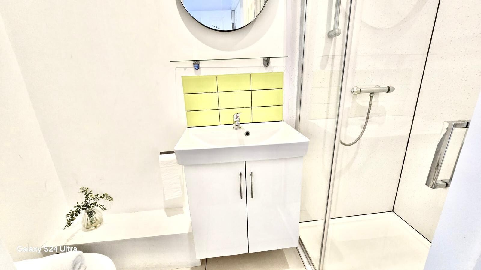 A modern bathroom with a white sink, yellow-tiled backsplash, and a glass shower enclosure.