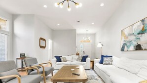 Un soggiorno moderno con un divano bianco, poltrone grigie, un tavolino in legno e un grande quadro astratto appeso al muro.