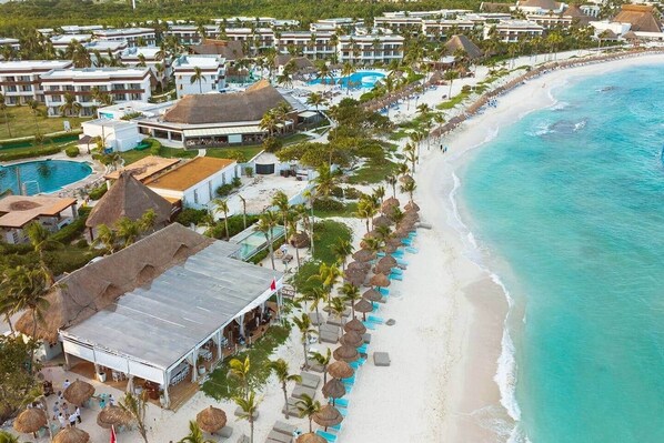 Vista aérea de um resort com acomodações na praia, uma piscina e uma praia com guarda-sóis.