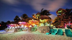 A beachside resort with thatched-roof structures, lounge chairs, and a sandy beach. - Akumal Alma | Walk to Beach | Sea View Roof Pools (Akumal)