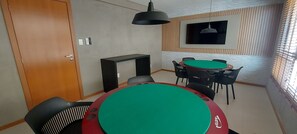 Ein Raum mit einem grünen Billardtisch, schwarzen Stühlen, einer Holztür und einem an der Wand befestigten Fernseher.