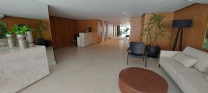 A modern hotel lobby with a reception desk, seating area, and potted plants. - COBAR0127 - Edifício Barra Premium (Salvador)