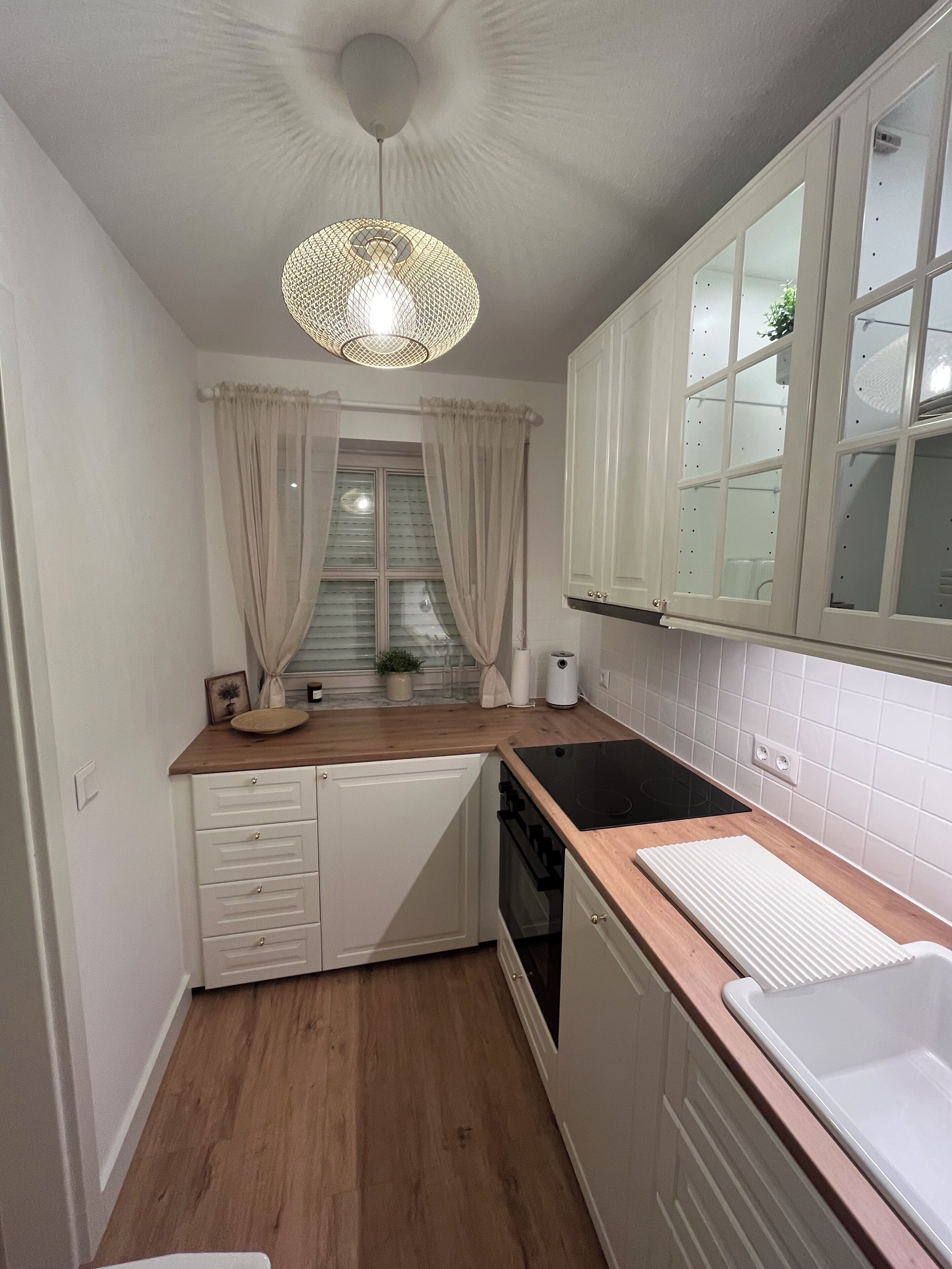 A compact kitchen with a wooden countertop, white cabinets, a black stove, and a hanging light fixture.