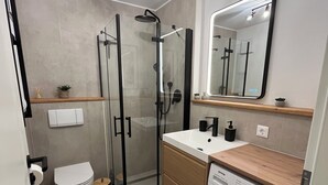 Ett modernt badrum med en dusch som är avskärmad med glasväggar, en toalett, ett handfat med spegel och en tvättmaskin.