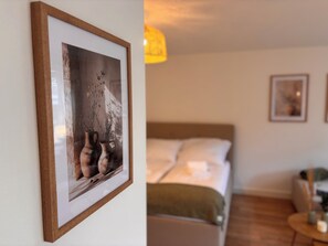 A framed photograph of vases with flowers on a wall, a bed with pillows, and a small round table with a candle. - Feel good at Stadtpark GZ - central & stylish (Günzburg)