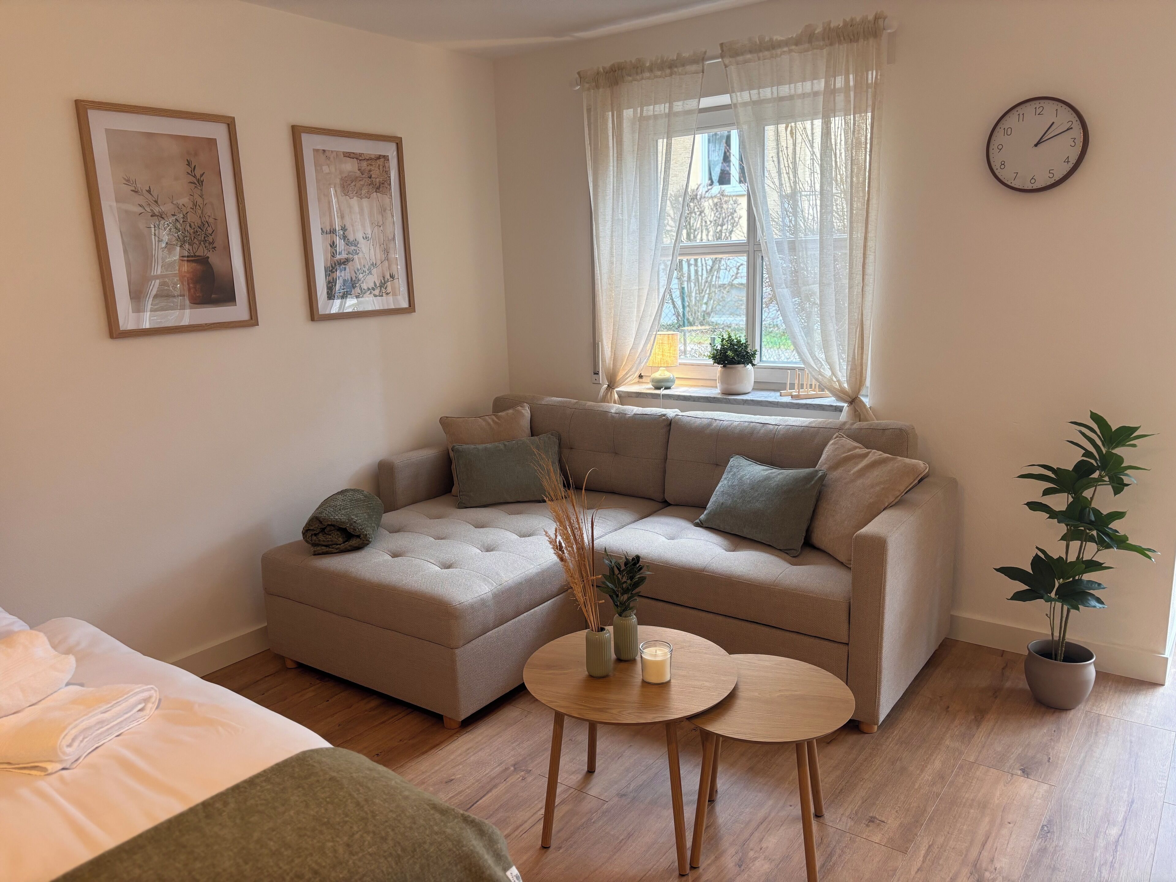 A cozy living room with a beige sectional sofa, a small round table with candles, and a potted plant.