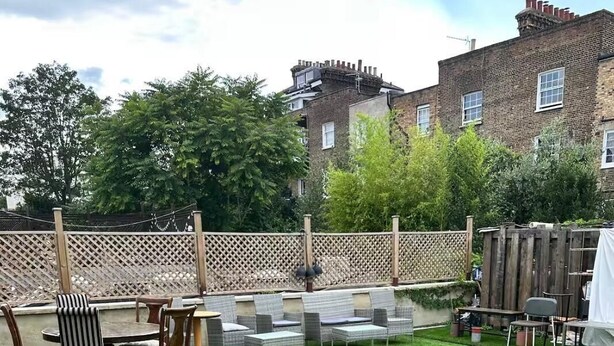 A backyard with artificial grass, a wooden fence, and outdoor furniture including chairs and a table. - Room 6 in Camden Parkway (London)