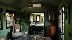 Une pièce avec une grande plante en pot, une chaise, un meuble en bois et un lit à l’arrière-plan.