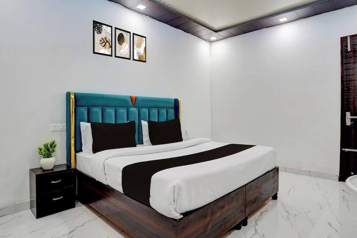 Une chambre à coucher moderne avec une tête de lit recouverte d’un tissu turquoise, une couvre-lit blanche et une petite table de chevet agrémentée d’une plante.
