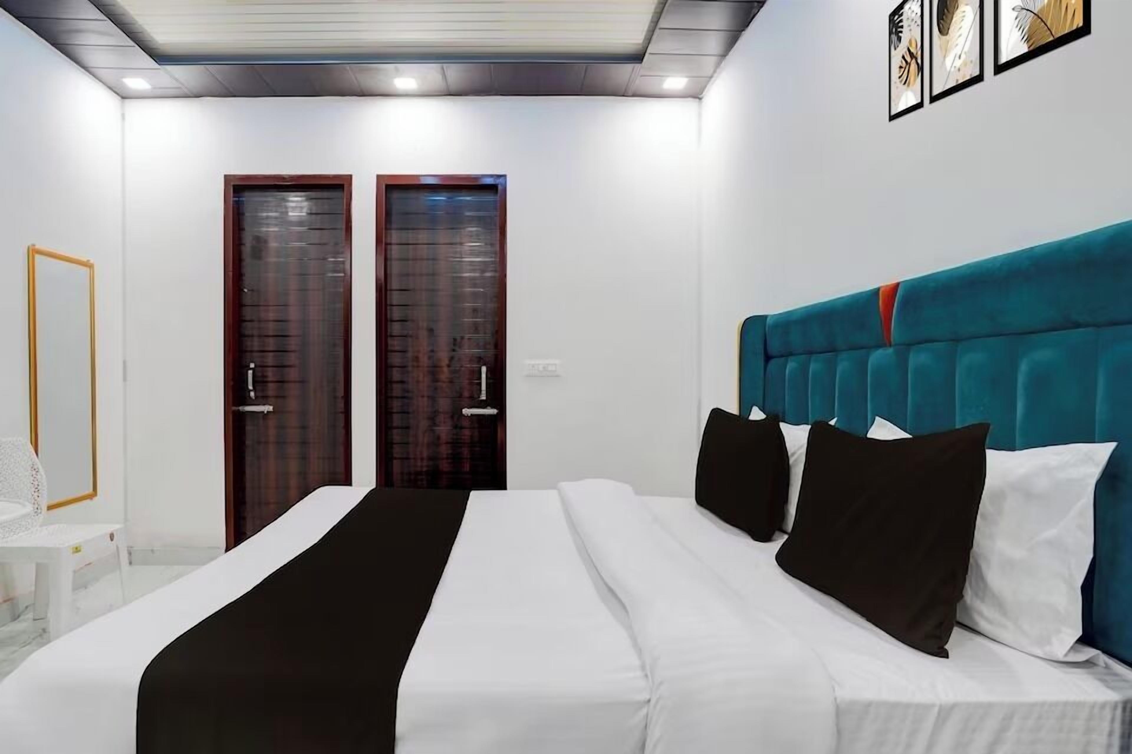 A hotel room with a bed, two doors, a white chair, and a framed picture on the wall.