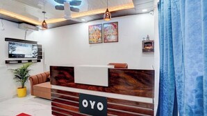 A reception area with a wooden reception desk, a television mounted on the wall, and a potted plant. - Hotel Brothers  (Dera Bassi)