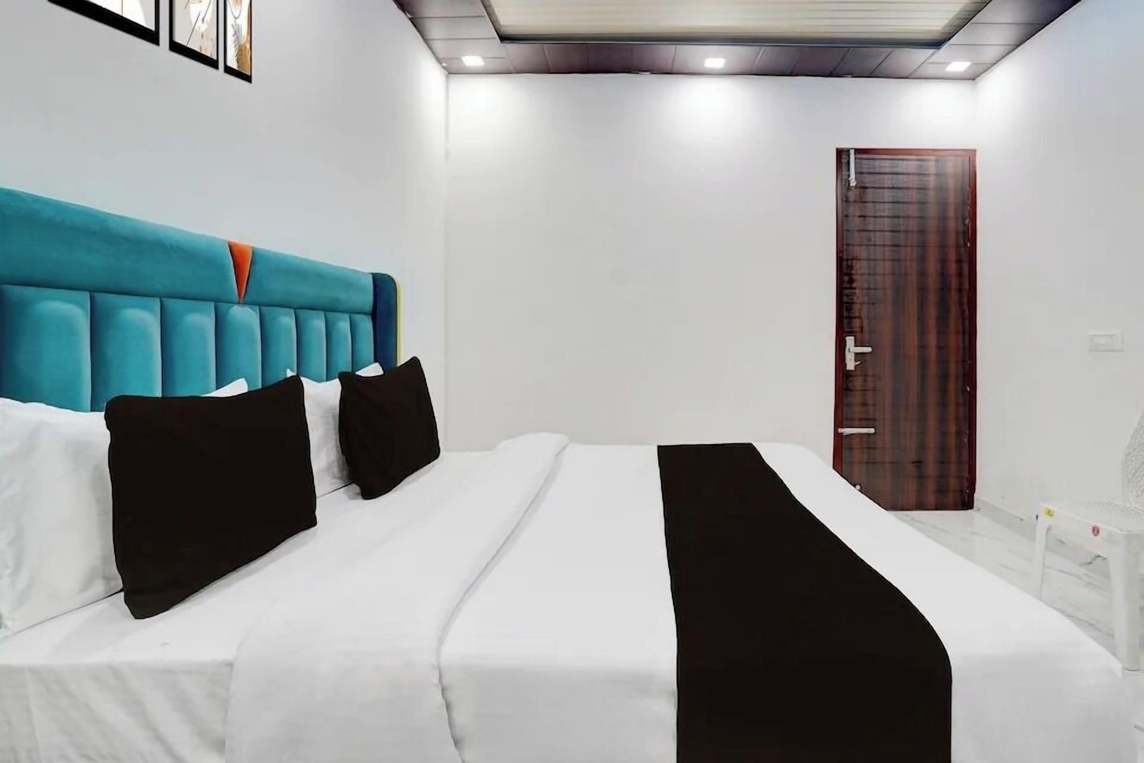 Una habitación de hotel con una cama grande, ropa de cama blanca, almohadas negras, un cabecero color turquesa y una puerta de madera.