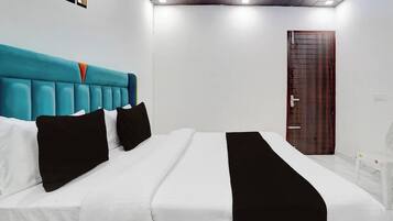 Una habitación de hotel con una cama grande, ropa de cama blanca, almohadas negras, un cabecero color turquesa y una puerta de madera.