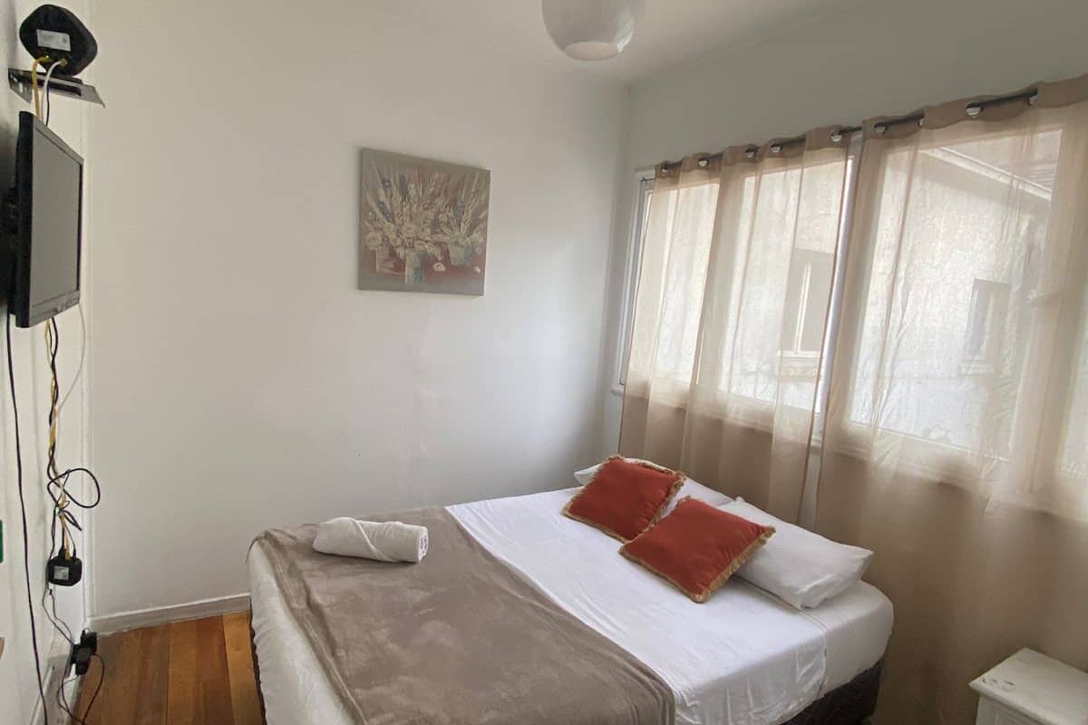 Een slaapkamer met een bed, een schilderij, een plafondlamp en een raam met gordijnen.
