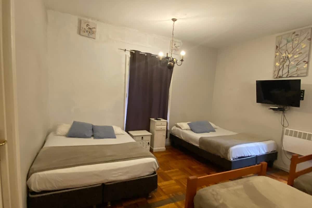 Een kamer met twee bedden, een houten vloer, een televisie aan de muur en een raam met gordijnen.