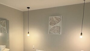 Un lit bien fait, avec du linge de lit blanc et un plaid gris, deux tables de chevet avec des lampes, et une œuvre d’art accrochée au mur au-dessus du lit.