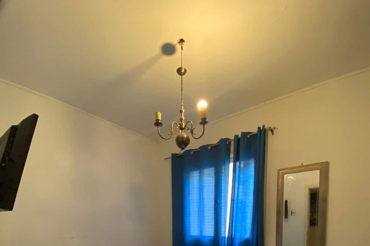 Een slaapkamer met een bed, een kroonluchter, een spiegel en een blauw gordijn.