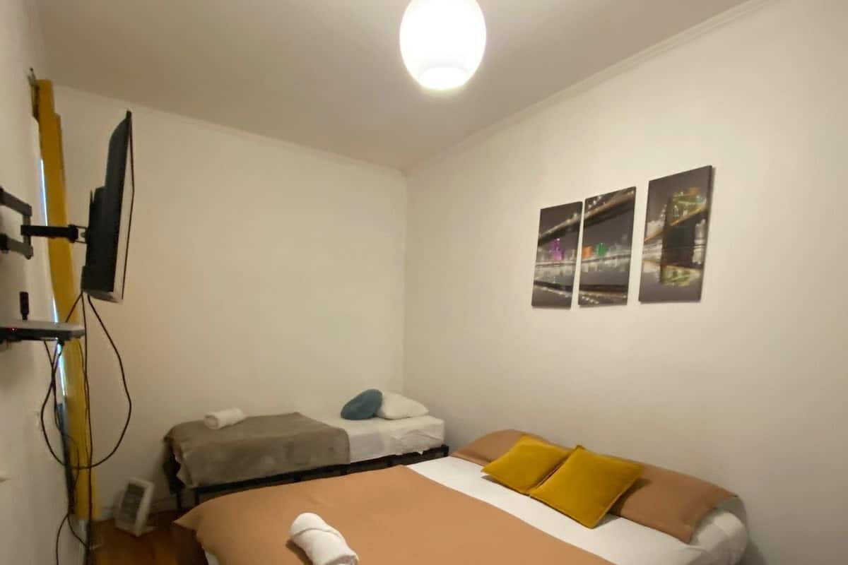 Een ruime, goed verlichte kamer met een bed, een bureau met een computer en een tv aan de muur.