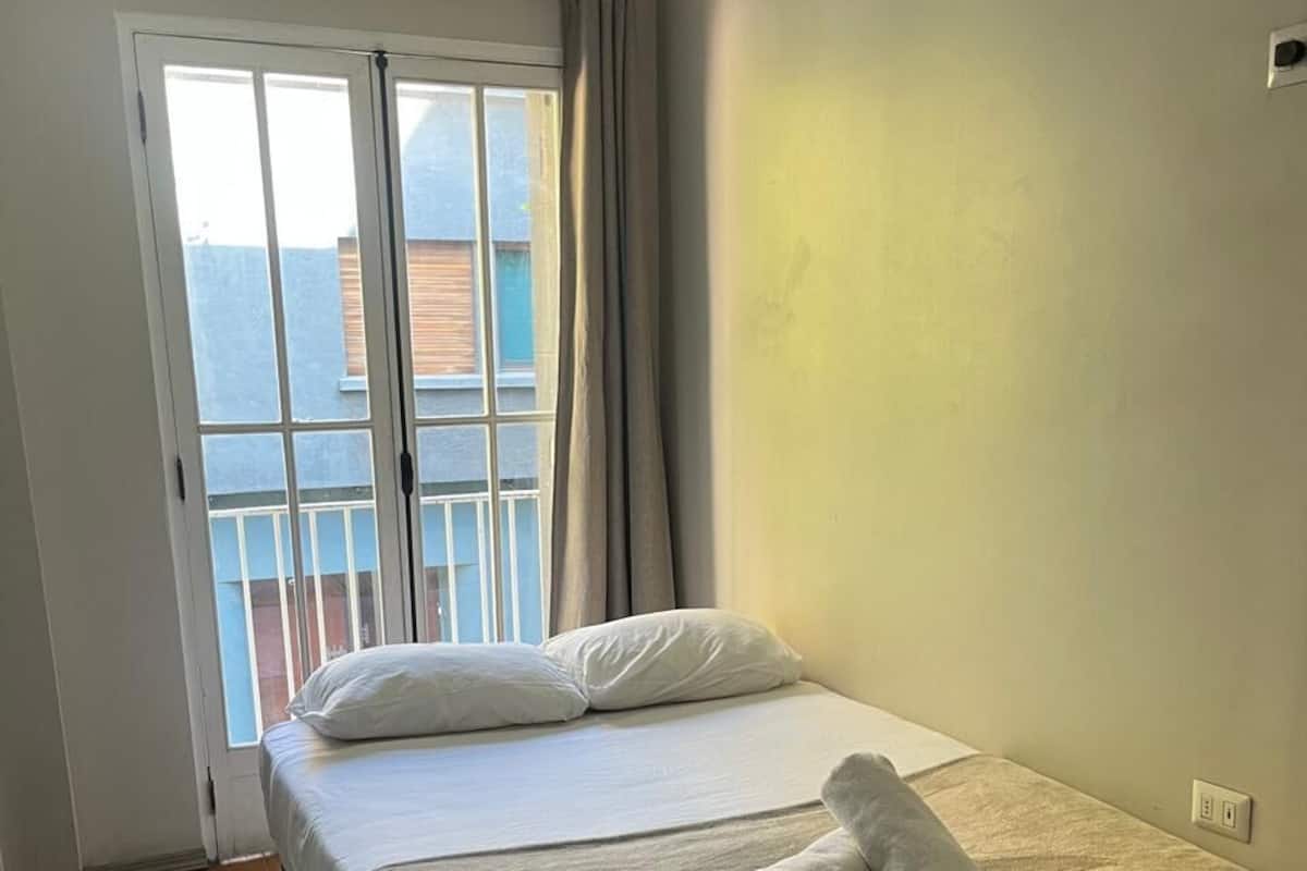 Een slaapkamer met een bed, een raam met gordijnen en uitzicht op de omgeving.