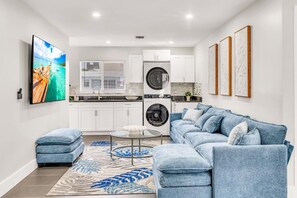 A modern living room with a blue sofa, a coffee table, and a TV on the wall.