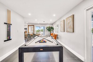 A pool table in a modern room with a dining area and artwork on the walls.