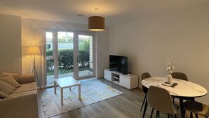 Una sala de estar moderna con un sofá, una mesa de comedor con sillas, un televisor y un gran ventanal.