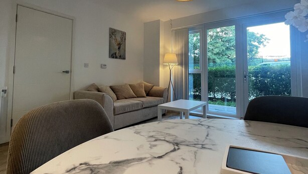Una sala de estar moderna con una mesa de centro de mármol, un sofá, una lámpara y vistas a zonas verdes por las ventanas.
