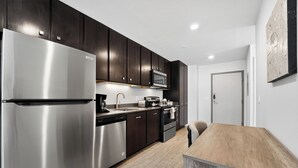A modern kitchen with dark cabinets, stainless steel appliances, and a wooden dining table. - Lux Studio ,Pool, Near St. Davids Hospital (Jarrell)