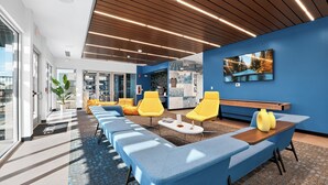 A modern lounge area with blue seating, wooden accents, and a large TV screen on the wall. - Lux Studio ,Pool, Near St. Davids Hospital (Jarrell)