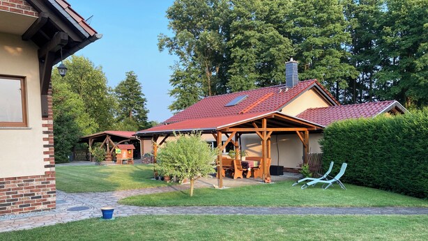 Uma casa com telhado de telhas vermelhas, varanda coberta e gramado bem cuidado.