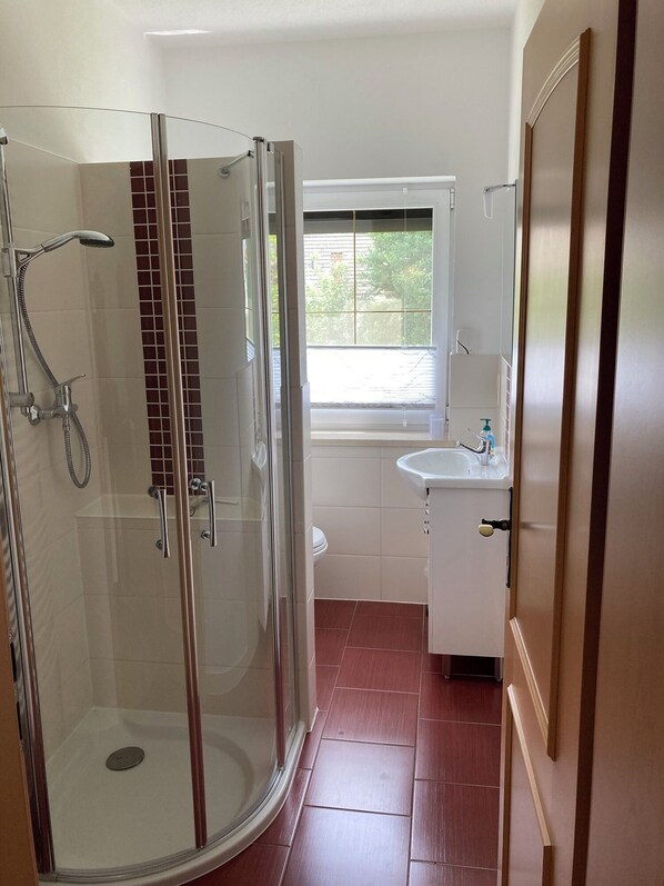 Un baño con ducha de vidrio, ventana, lavamanos y espejo.