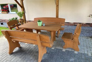Une table et des bancs en bois, destinés à l’extérieur, avec une plante en pot et un petit récipient posé dessus.