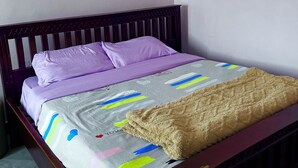 A bedroom with a wooden bed frame, purple bedding, and a grey bedspread with colorful patterns.