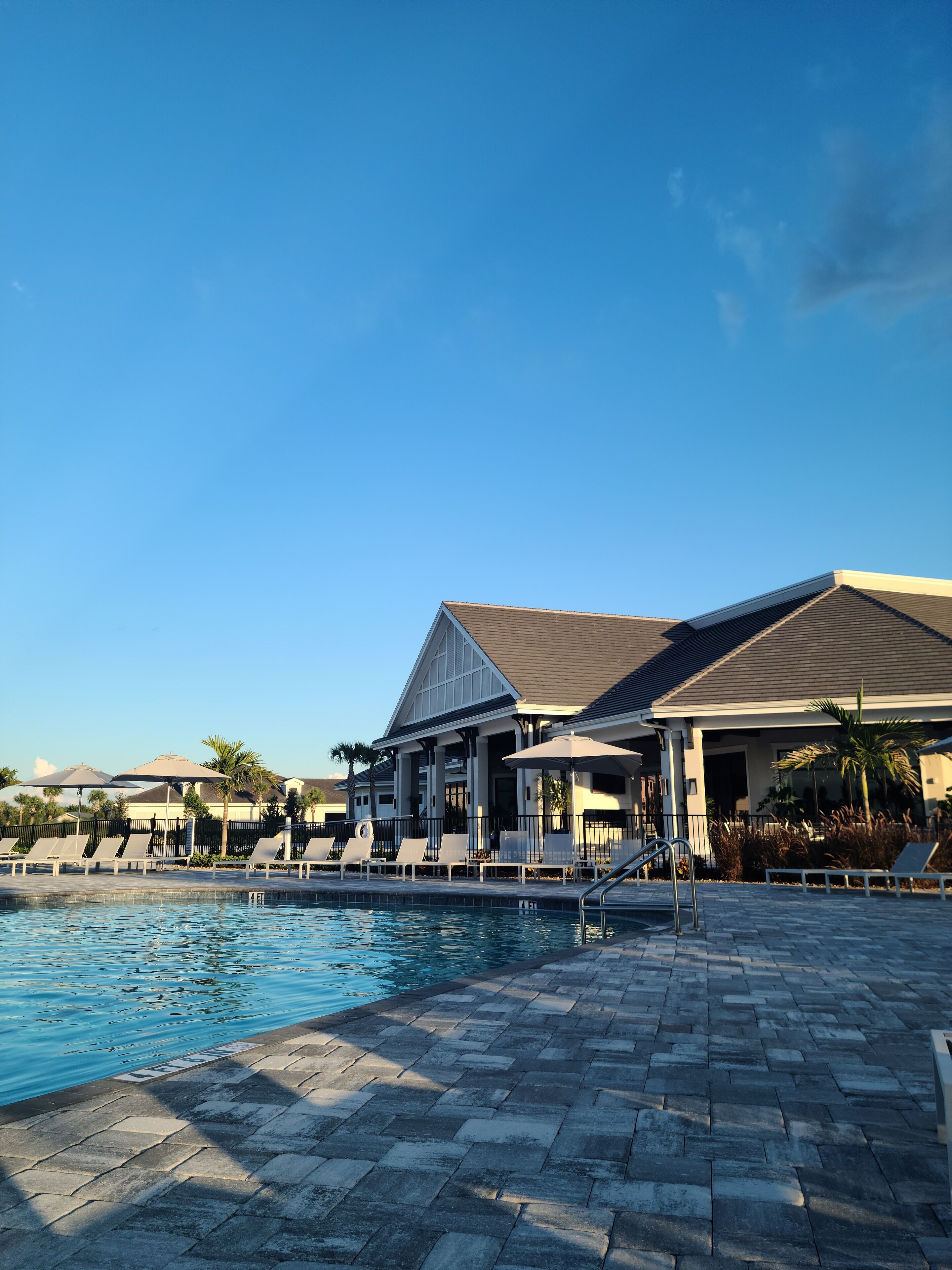 A pool area with lounge chairs and umbrellas, a clear blue sky, and a building with a sloped roof.